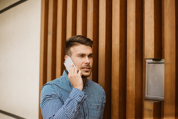 The guy in blue shirt talking on a phone in front of wooden wall