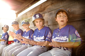 Little league team (8-9) cheering together in dugout