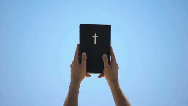 Man reaching out hands to sky holding bible, new testament, ten commandments