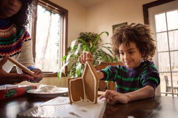 Boy (6-7) making gingerbread house with woman