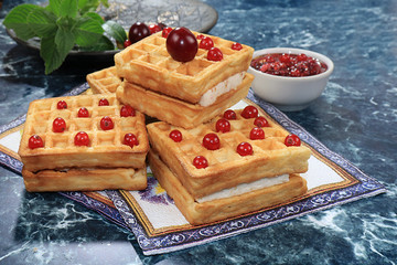 Crispy waffles with berries on a sunny table. Morning breakfast with waffles, currants and milk on a blue background,