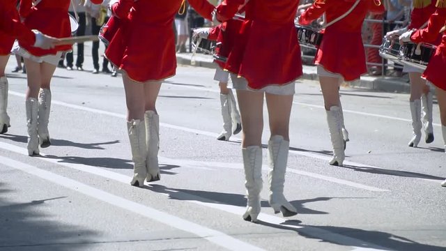 Street performance of festive march of drummers girls in red costumes on city street. Slow motion