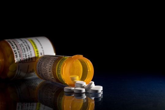 Oxycodone is the generic name for a range of opoid pain killing tablets. Prescription bottle for Oxycodone tablets and pills on glass table with reflections