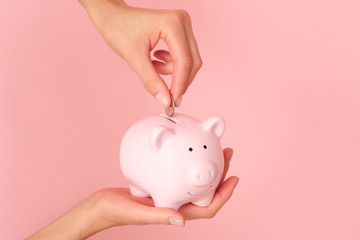 Femle hand isolated on pink background putting coins to the piggy bank.