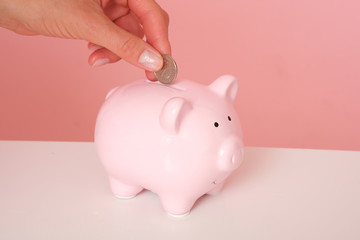 Femle hand isolated on pink background putting coins to the piggy bank.