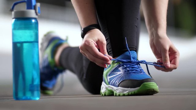 Close-up of overweight female jogger legs in sneakers and hands tying shoelaces during cardio training on city stadium track. Active fat woman runner tying shoelaces on sports shoes