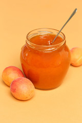 Jar of apricots jam and fresh apricots on an orange background