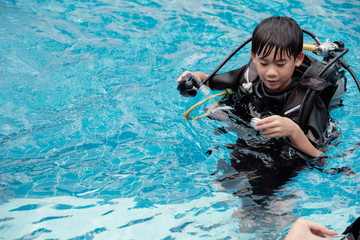 Young little Asian boy scuba diver checking pressure gauge and holding regulator, diving lessons...