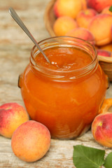Jar of apricots jam and fresh apricots on wooden background