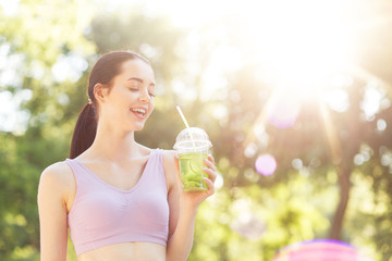 Young beautiful girl drinking green beverage with lime and kiwi from plastic cup take-out food....