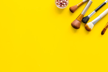 Women desk with brushes and blusher for make up on yellow background flat lay space for text