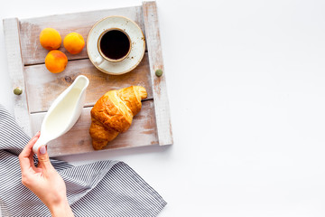 Breakfast on the tray in hands with croissant, coffee with cream and fruit on white background top view mock up