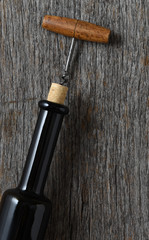 Naklejka premium Wine bottle on a rustic wood table with an antique corkscrew inserted in the cork pulled partially out