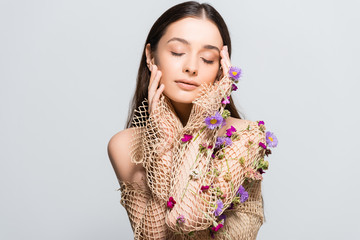 beautiful woman with closed eyes in mesh beige clothing with purple flowers touching face isolated on grey with copy space