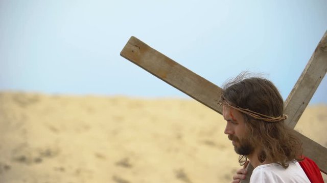 Jesus in crown of thorns carrying heavy cross, sacrifice for sinners salvation