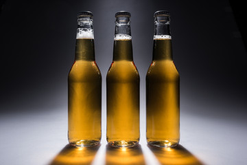 three glass bottles with beer on dark background with back light
