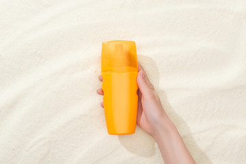 cropped view of woman holding orange sunscreen above golden sand