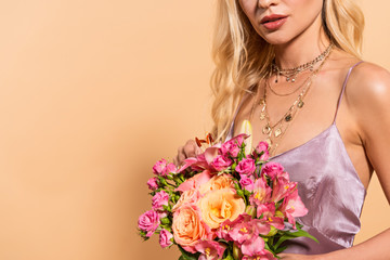 cropped view of elegant woman in violet satin dress holding bouquet of flowers isolated on beige with copy space