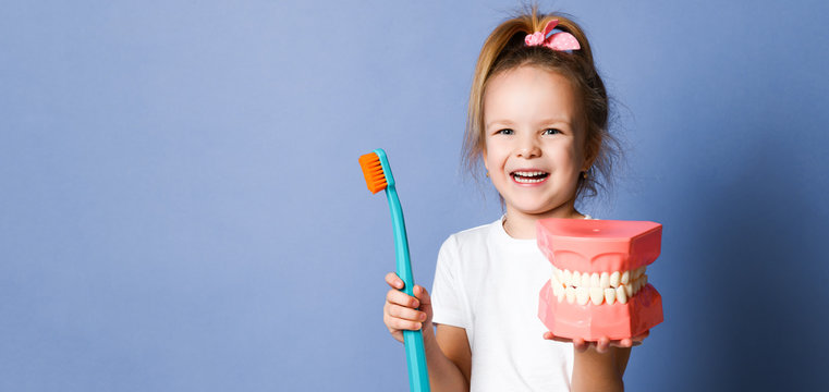 Happy Girl Kid And Big Dental Implant Model With Toothbrush Standing Laughing On Purple