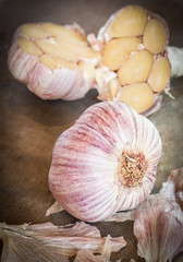 Bulbs of raw garlic laying on a cutting board with blur of cut garlic in the background.