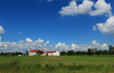 Beautiful blue sky with white clouds, green field, classic white and red farm house