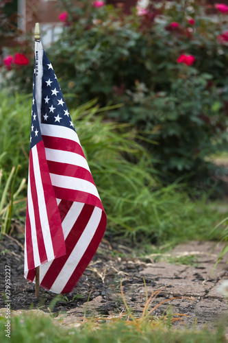 small flag in a garden with brick walkway in front of a rose bush