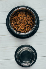 top view of metal bowl with pet food and empty bowl on wooden surface
