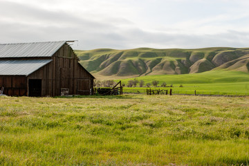 A wooden barn on a farm with green hills and pasture