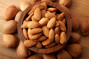 Almond snack, meal high in protein and healthy lifestyle concept thee with a brown wooden bowl of unscheduled almonds on rustic wood table surrounded by raw nuts still in shell