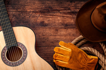 American culture, living on a ranch and country muisc concept theme with a cowboy hat, acoustic guitar, farm gloves and a rope lasso on a wooden background in a old saloon with copy space