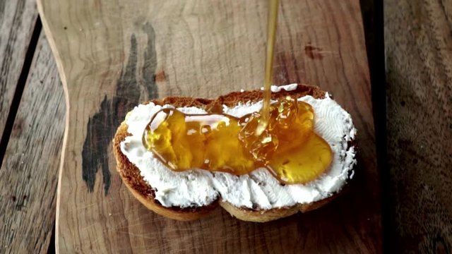 Pouring honey to fried bread with spreadable cheese.