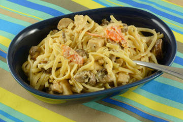 Chicken, tomatoes and mushrooms in cream sauce over linguine pasta in blue dish on striped place mat