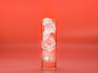 Glass full of ice cubes on pink background, close up view. Pieces of solid water in glass photographed while melting down. Selective soft focus. Blurred background