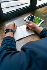 Human hand holding pen and writing next to tablet