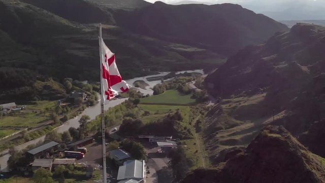 Dynamic shot of Georgian National Flag Waving over Mountains, Hills and Houses in Georgia, fast moving Aerial Close Up shot