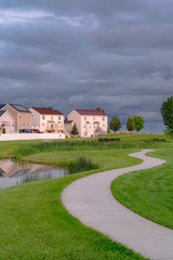 Fototapeta na wymiar Neighborhood park with pond bridge and pathway under sky with thick gray clouds