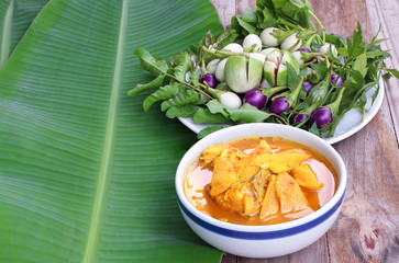 Top view of Thai hot and sour spicy yellow soup and fresh sea fish in the white bowl with vegetable ,on banana leaf and wooden table , With copy space..