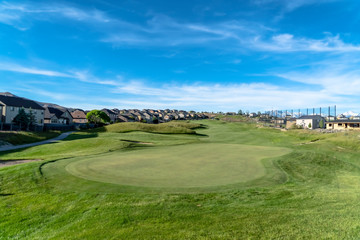 Golf course with view of lovely homes and mountain under blue sky with clouds