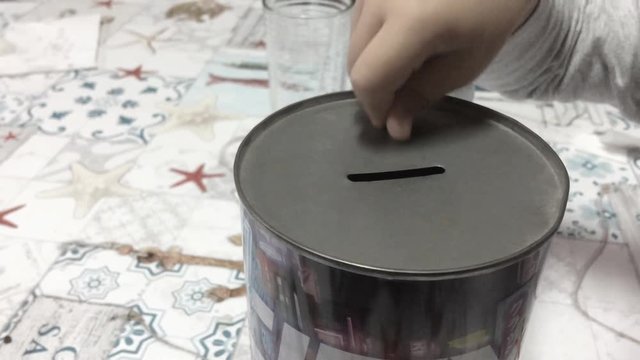 Young boy child toddler inserting a coin into a tin foil money saving piggy bank financial investment  future savings