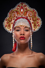Fashionable portrait of a woman with the red lipstick on full lips. Studio shoot of an african american female model with the richly decorated kokoshnik on her head. Russian style, culture