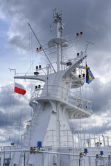 Naklejka premium Satellite and communication equipment tower or mast on a large cruise ship with aerials and antennae against cloudy sky.