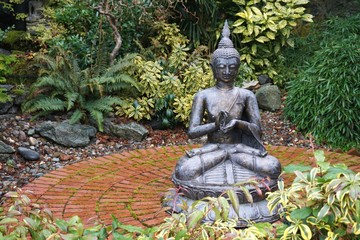 Seated Buddha statue on a round brick patio amid lush green garden