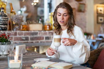 thoughtful, melancholic girl drinks latte coffee for breakfast in cafe. Quiet calm morning atmosphere. Delicious breakfast.