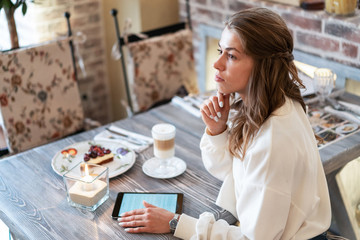 thoughtful girl reads an e-book during breakfast in cafe. Work on tablet during break. Freelance. Creative person. Coffee Latte, Cheesecake, Candle Light