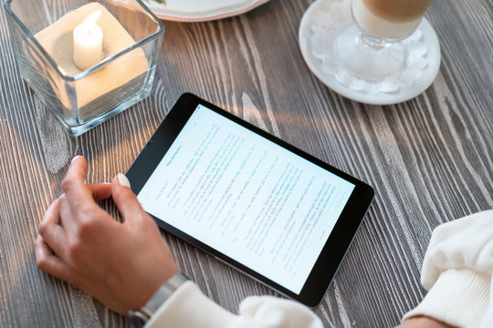 Girl Reading E-book At Breakfast In A Cafe. Read The Text From The Tablet Computer At A Table In A Cozy Restaurant. Traction Reading Knowledge