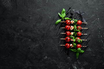 Cherry tomatoes, mozzarella and basil. On a black stone background. Italian cuisine. Top view. Free space for your text.