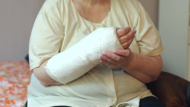 Close-up of the broken arm of an elderly woman. Hand in a cast in a woman. An elderly woman with a broken arm is sitting at home on the couch. High resolution.