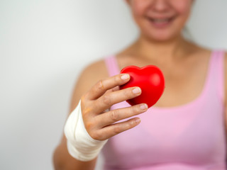 Women with hand injury and bandage holding red heart with smile
