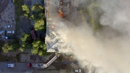 The roof of a residential house is burning. firefighters with a ladder extinguish a fire on the...