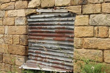 A rusty corrugated metal sheet against a stone building